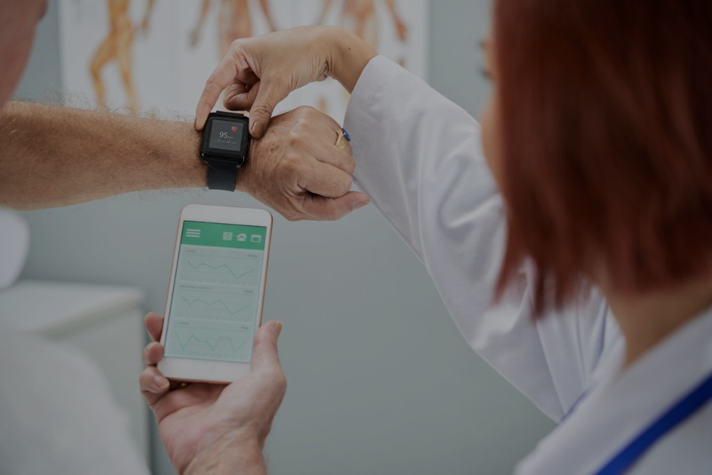 Doctor assisting a patient with a SMART watch and a mobile app, to monitor the patient's health