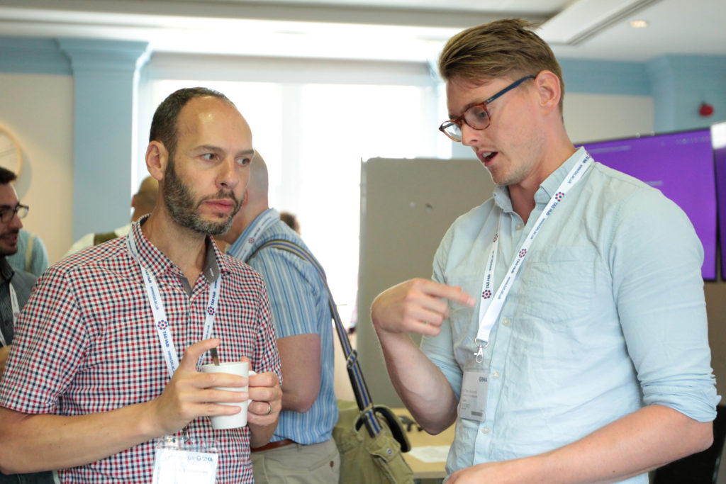 Two male delegates in discussion, one holds a coffee cup