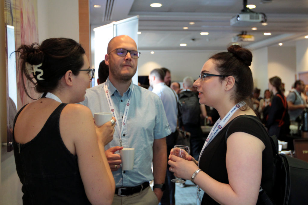 Two female and one male attendee in discussion holding coffee mugs