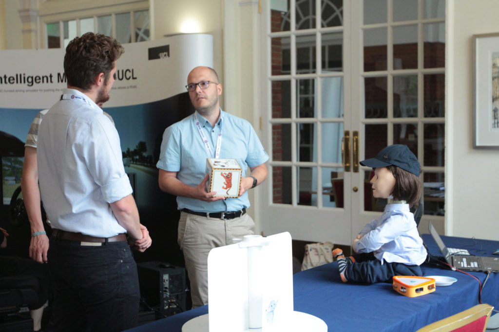 Delegates and exhibitor discuss how to interact with the robot child figure seated on the table