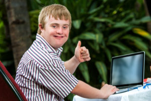 Young teen with downs syndrome using a laptop, smiling