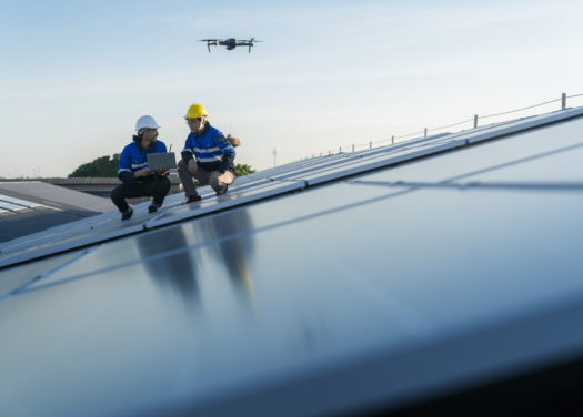 Specialist technician professional engineercontrol drone checking top view of installing solar roof panel on the factory rooftop under sunlight. Engineers holding tablet check solar roof.