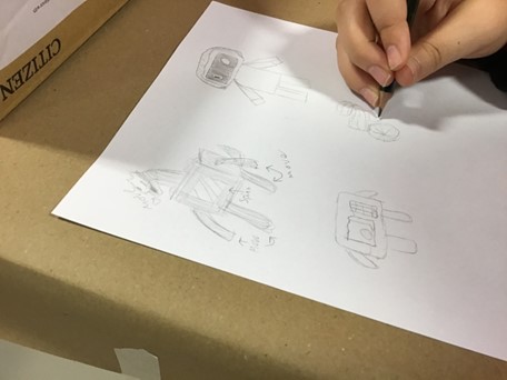 A child's hand holding a pencil, doodling robots onto a white piece of paper